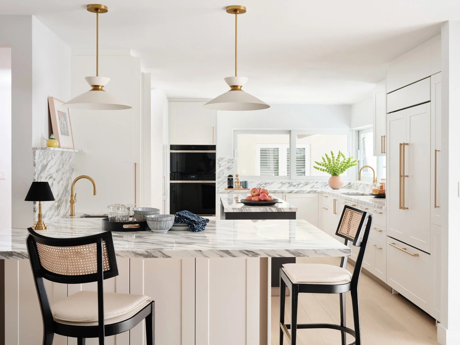 Kitchen island with black counter stools and brass pendants