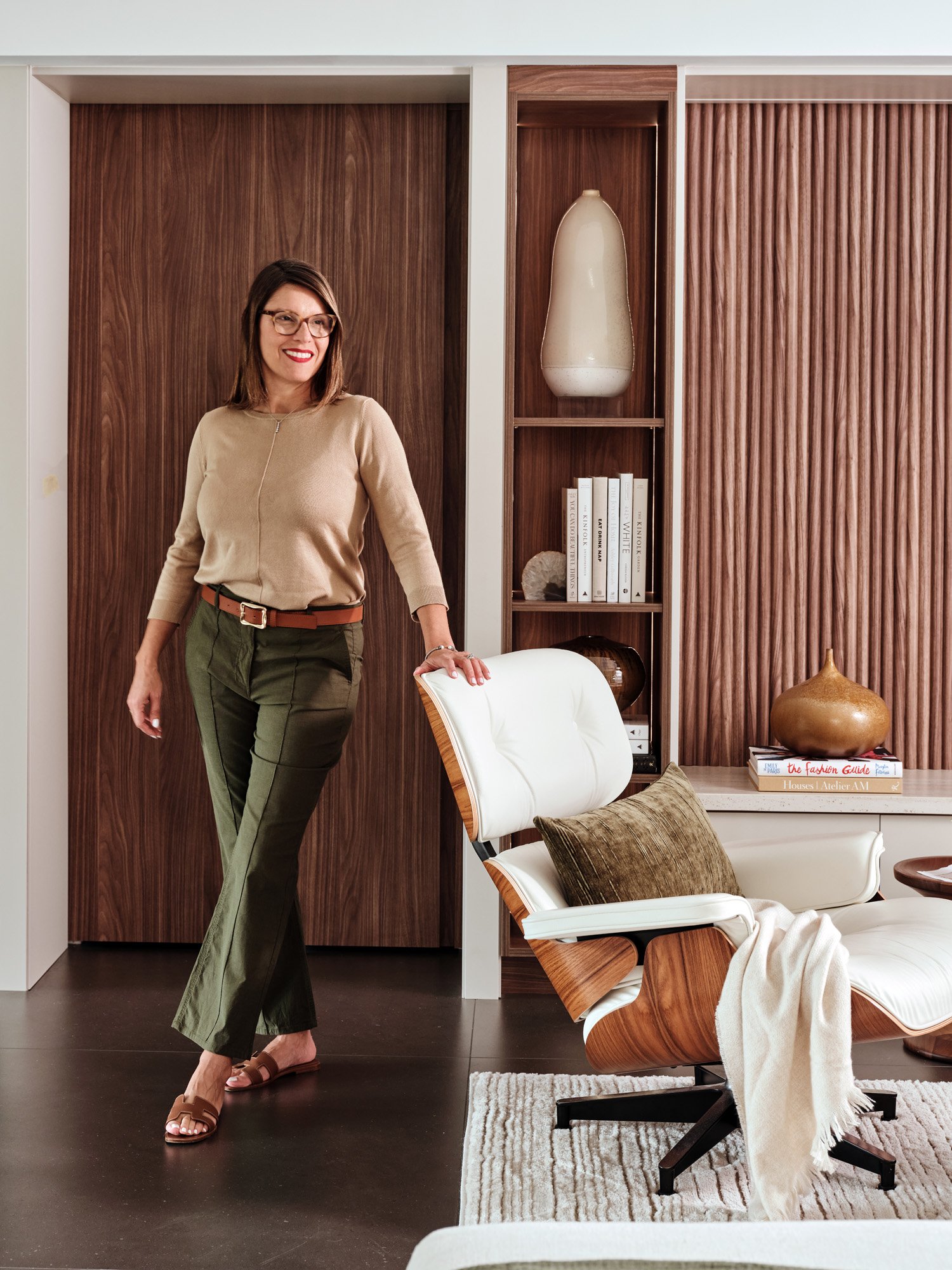 Interior designer Adriana Jacir beside a leather lounge chair and walnut wall