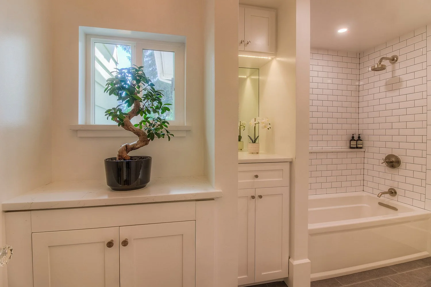 White vanity under a window with bonsai plant and tub beyond