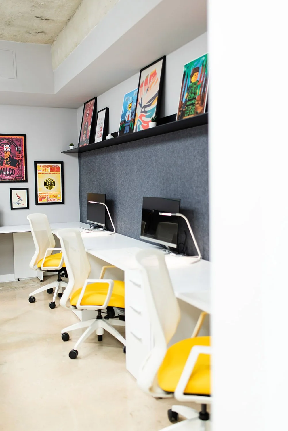 Row of desks with yellow chairs and framed art on a dark wall