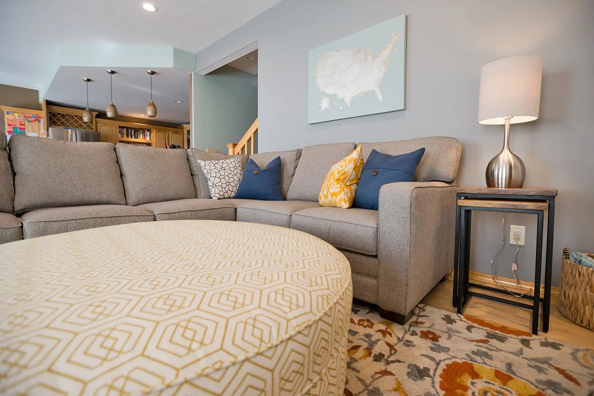 Gray sectional with round ottoman and coastal artwork