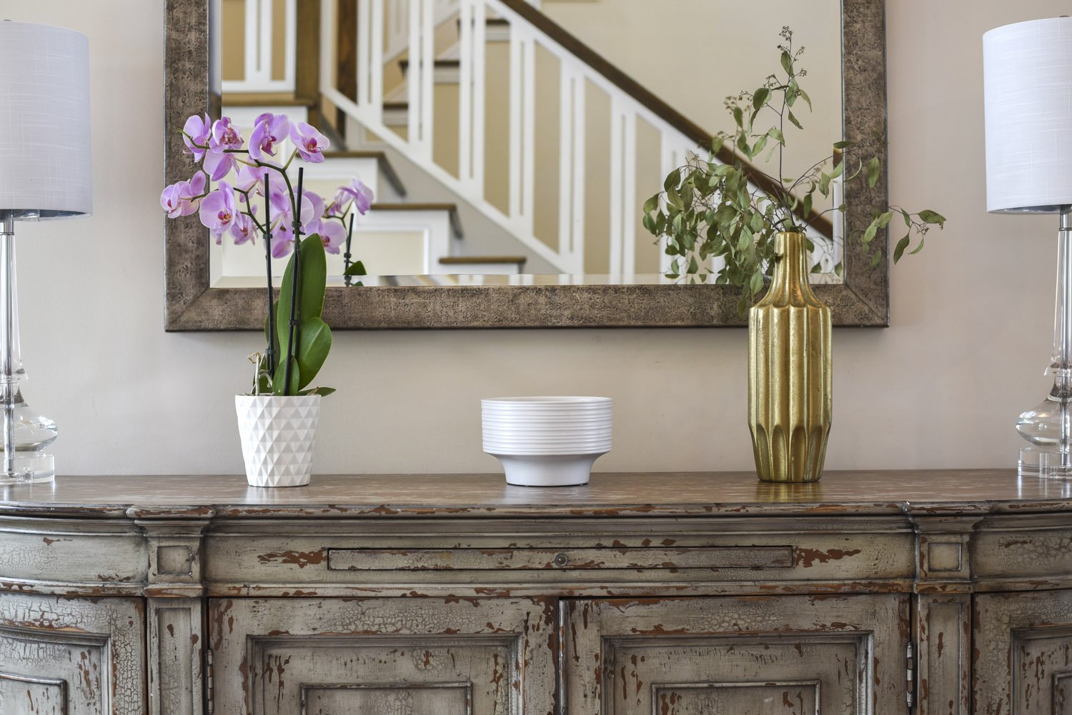 Wood console with purple orchid, gold vase and framed mirror