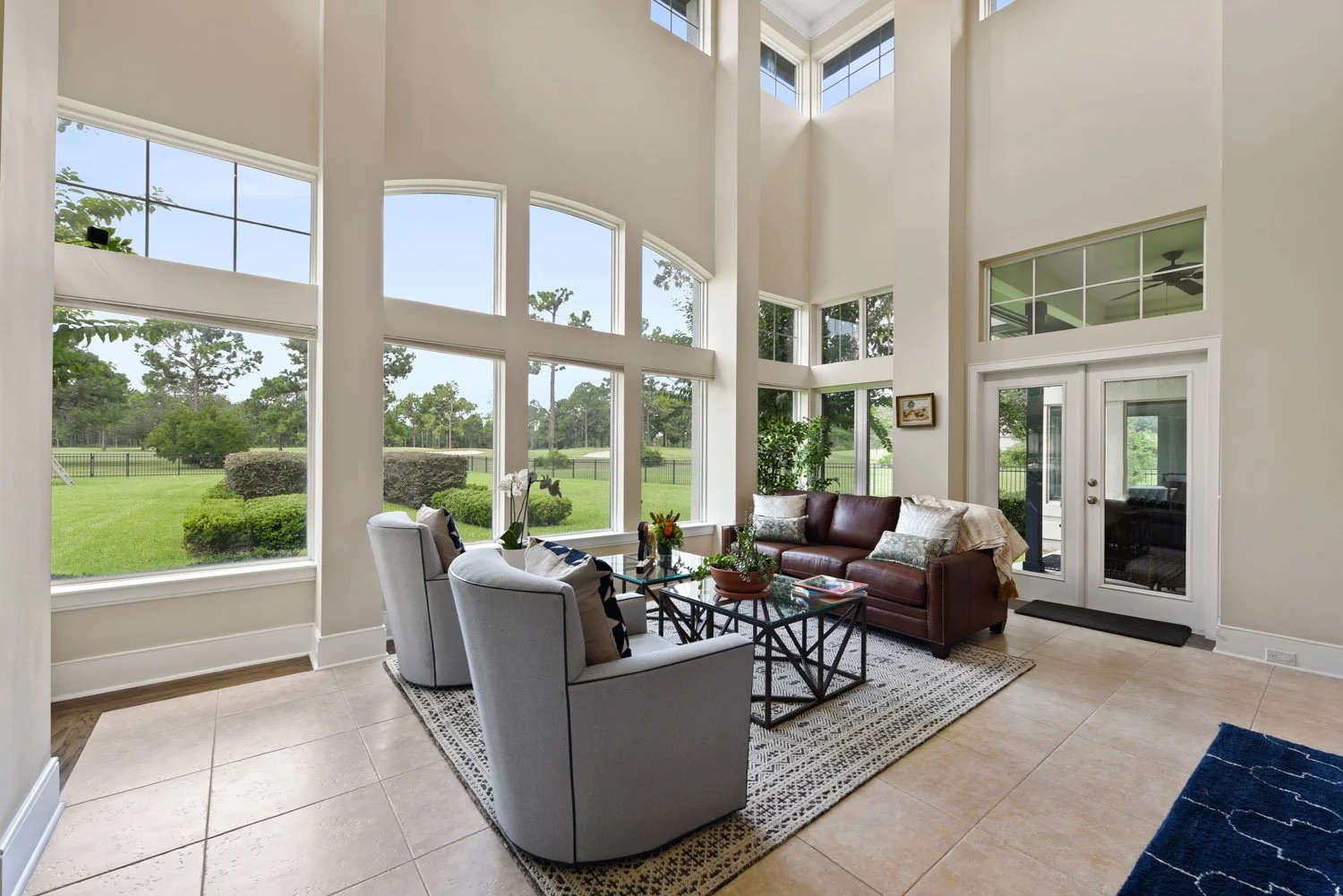 Seating area with gray swivel chairs and tall windows to the golf course