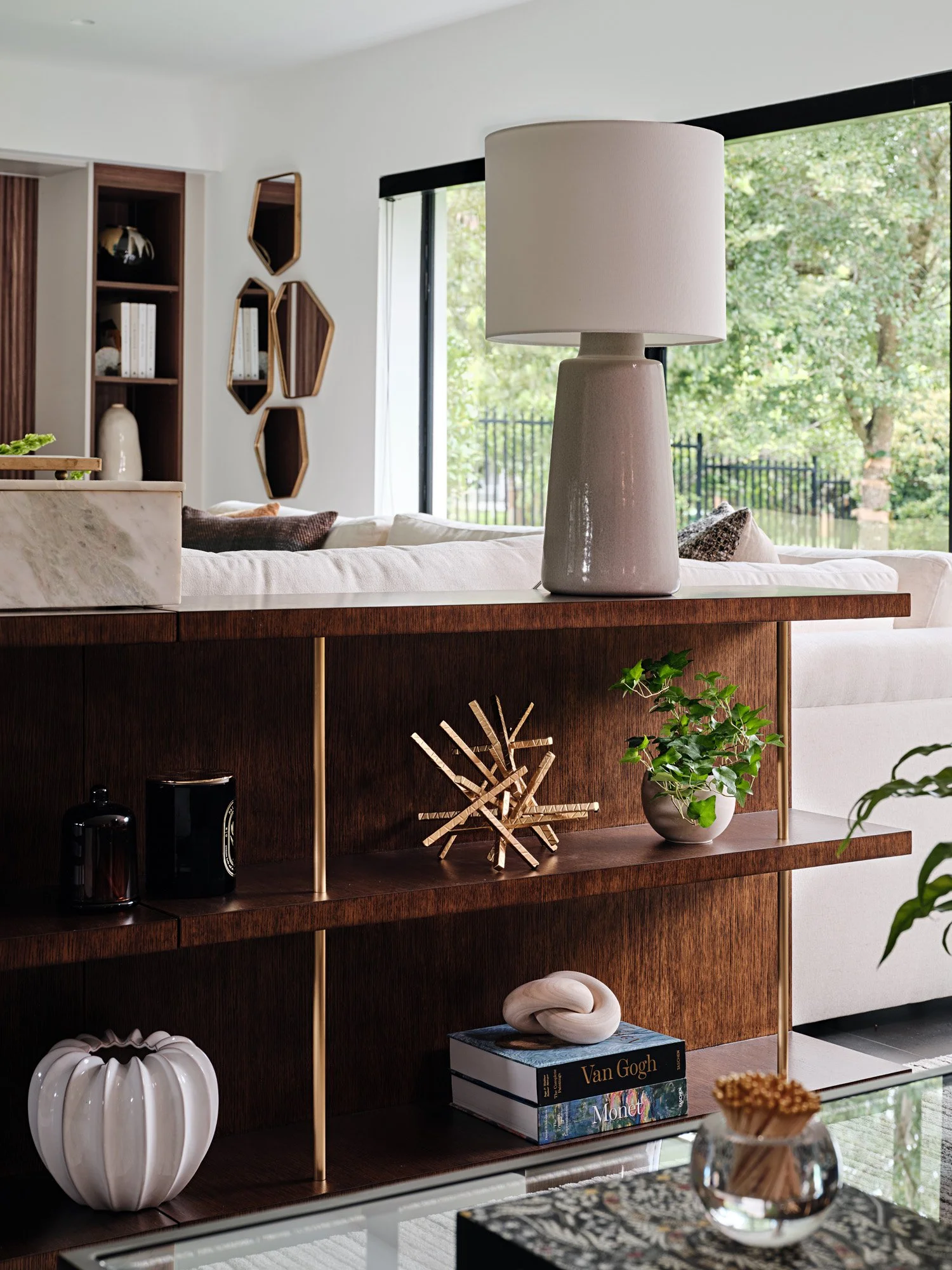 Walnut open shelving with ceramic lamp and decor behind a sofa
