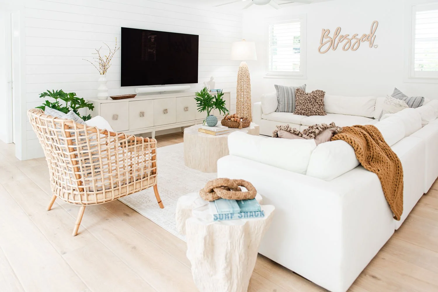 White sectional with rattan chair facing a wall-mounted TV