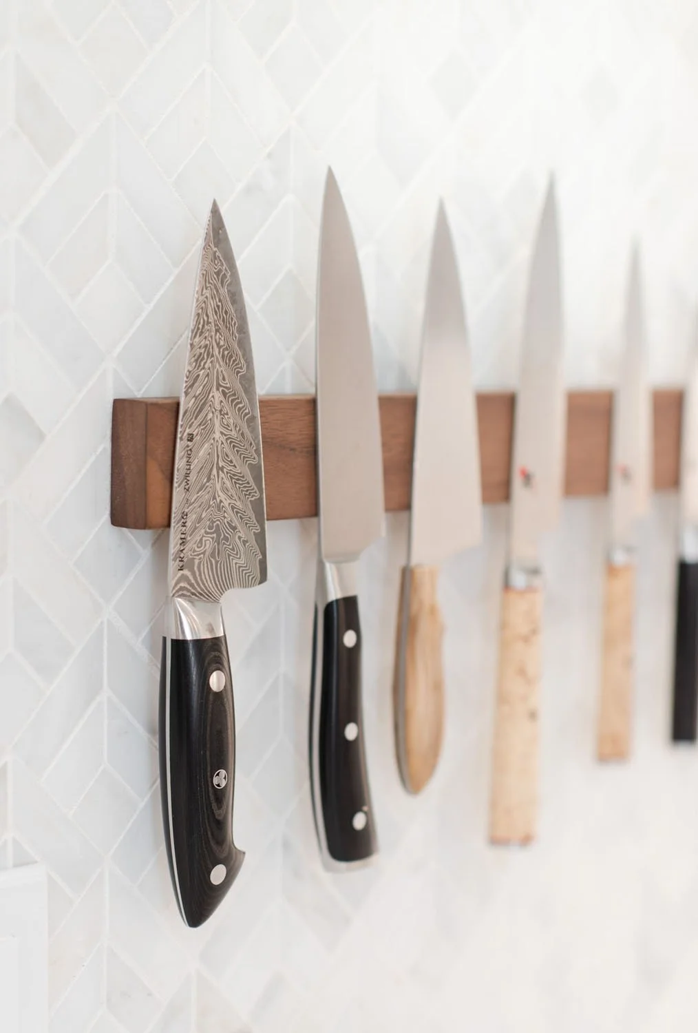 Chef knives on a magnetic strip against marble tile