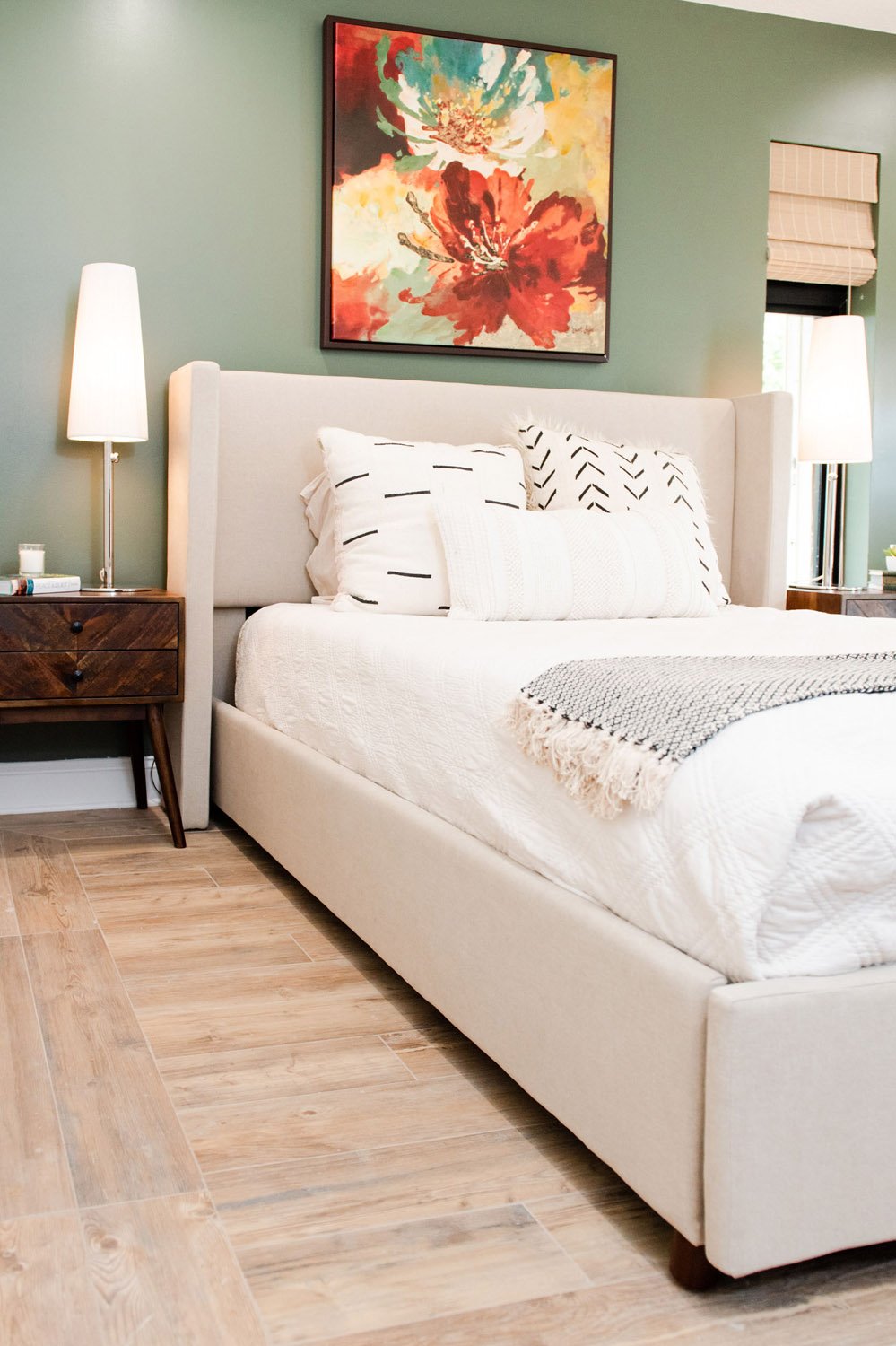 White upholstered bed with floral artwork and tall table lamp