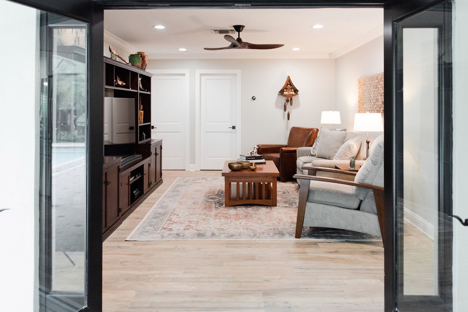 Black French doors opening to a living room with ceiling fan