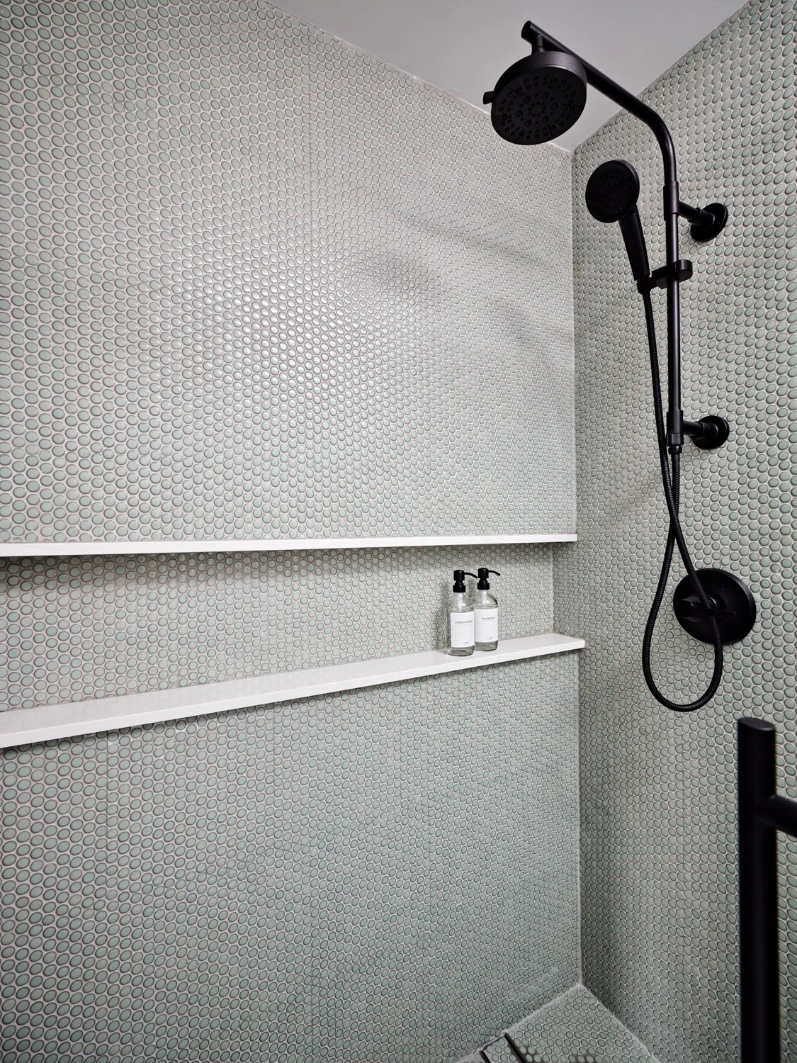 Shower with gray penny tile and black rain shower head
