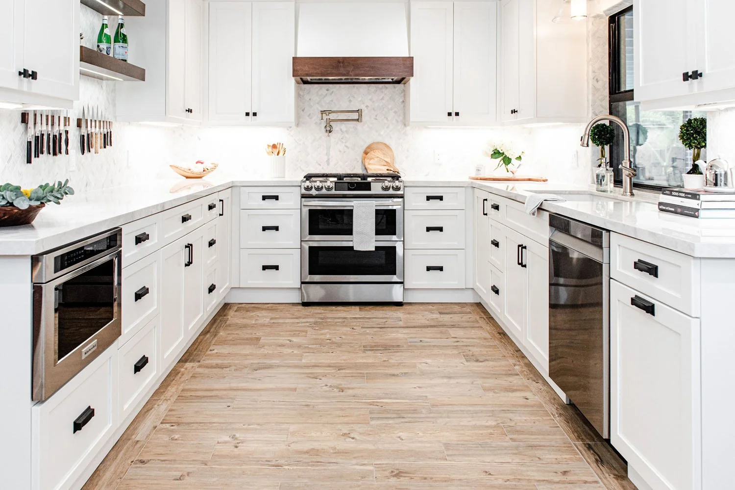 U-shaped kitchen with white cabinets, stainless appliances and wood-look tile