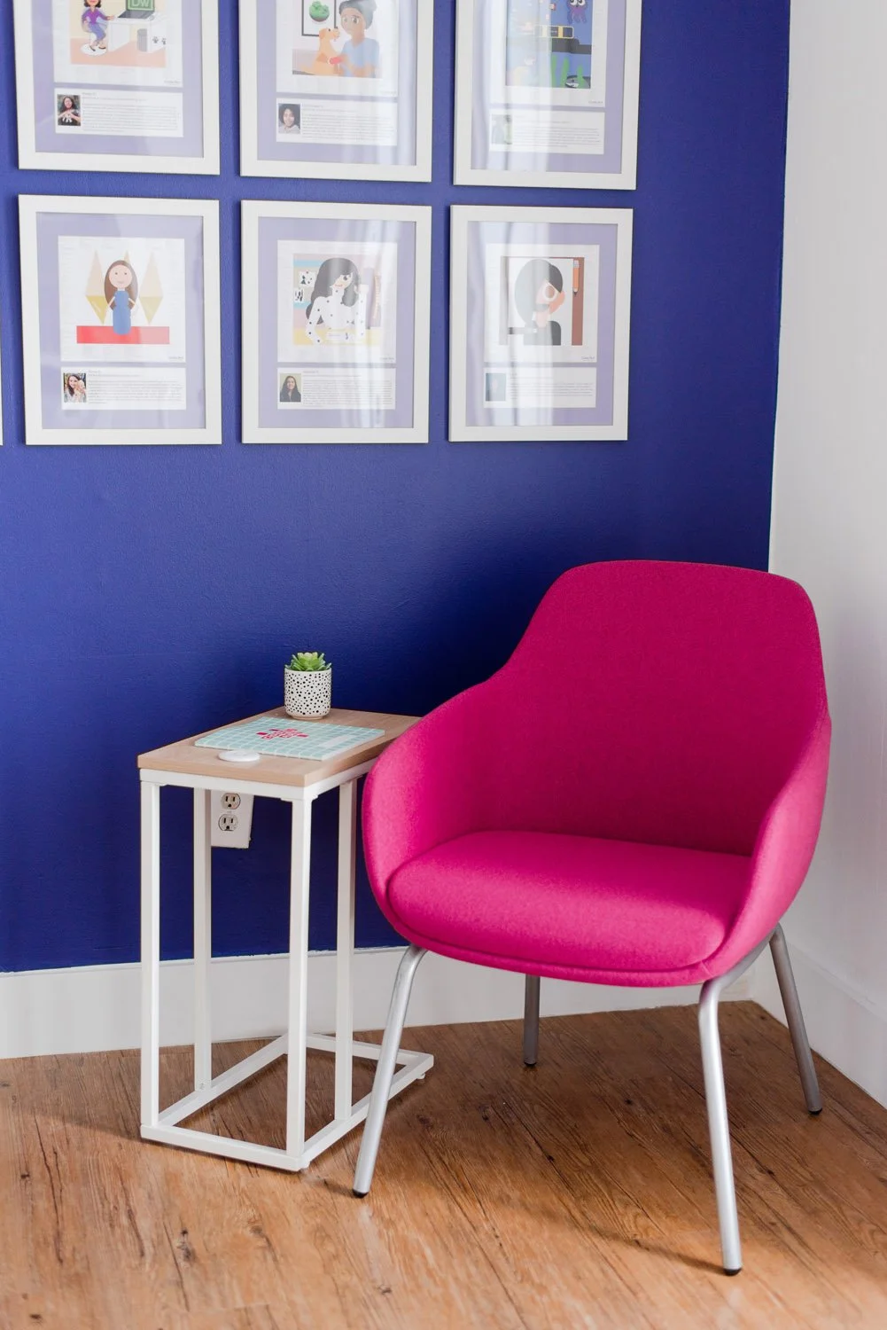 Pink accent chair in front of a navy gallery wall