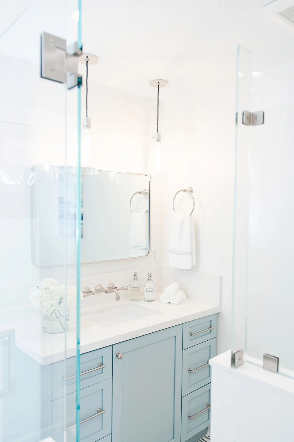 Light blue vanity seen through a frameless glass shower