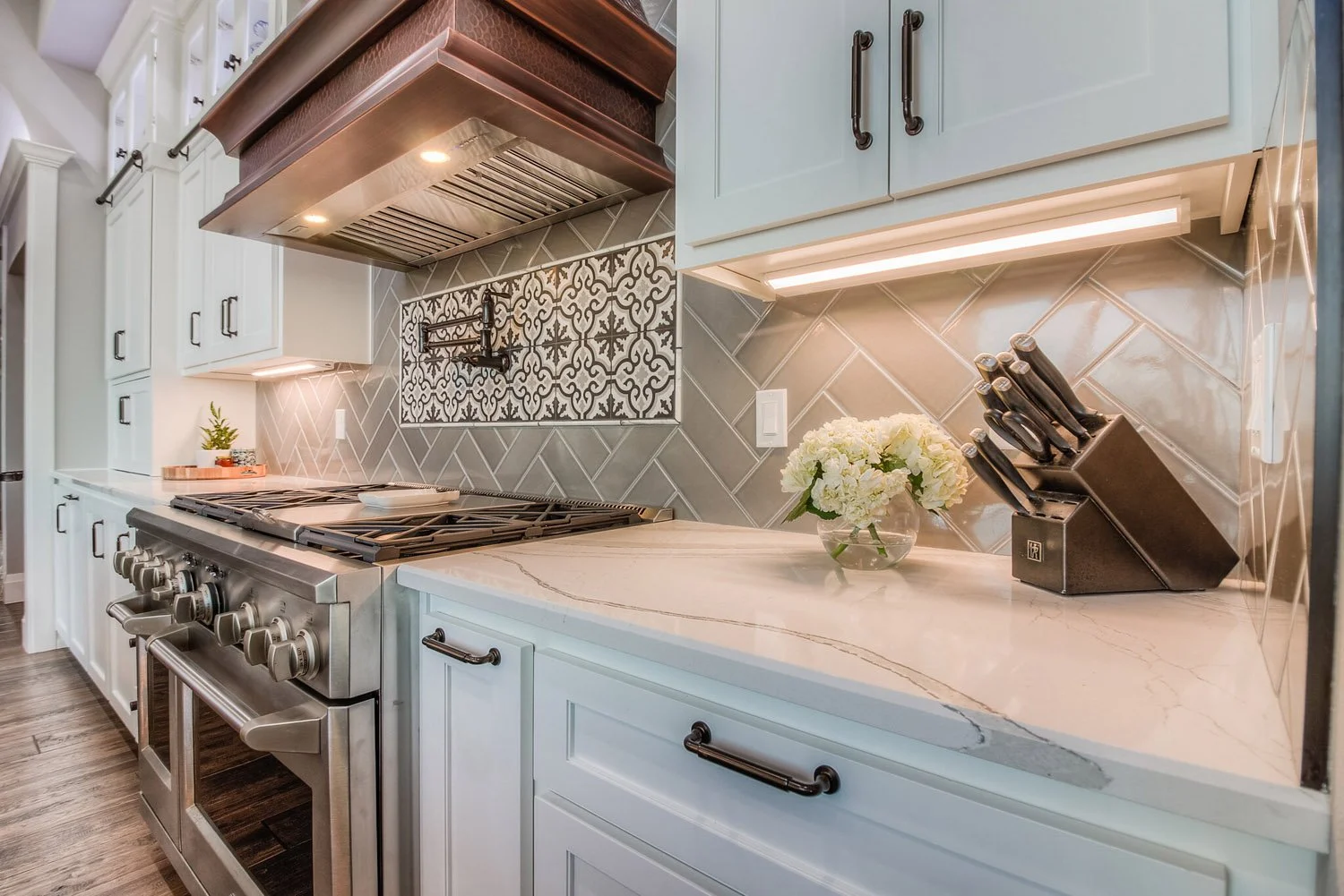 Range wall with wood hood, gray tile backsplash and white cabinets