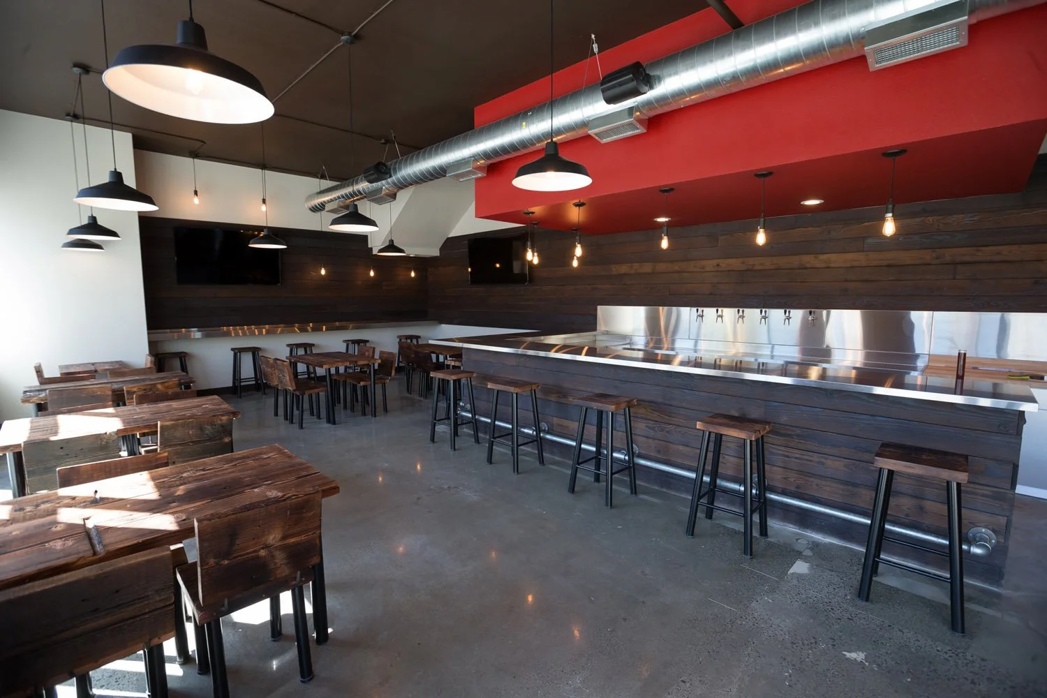 Brewery taproom with long bar, wood tables and red accent soffit