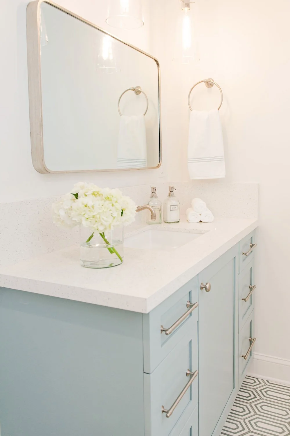 Light blue vanity with rounded mirror and white hydrangeas