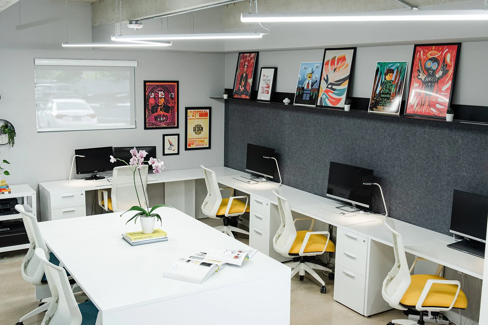 Office with white desks, yellow chairs and framed posters