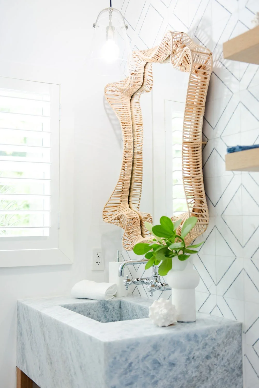 Marble pedestal sink under an ornate rattan mirror