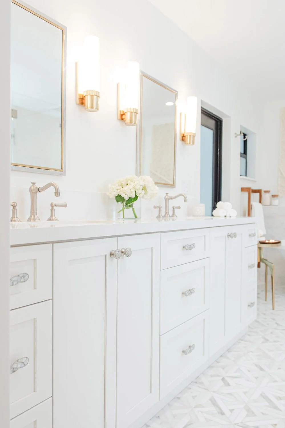 White double vanity with marble floor and brass sconces