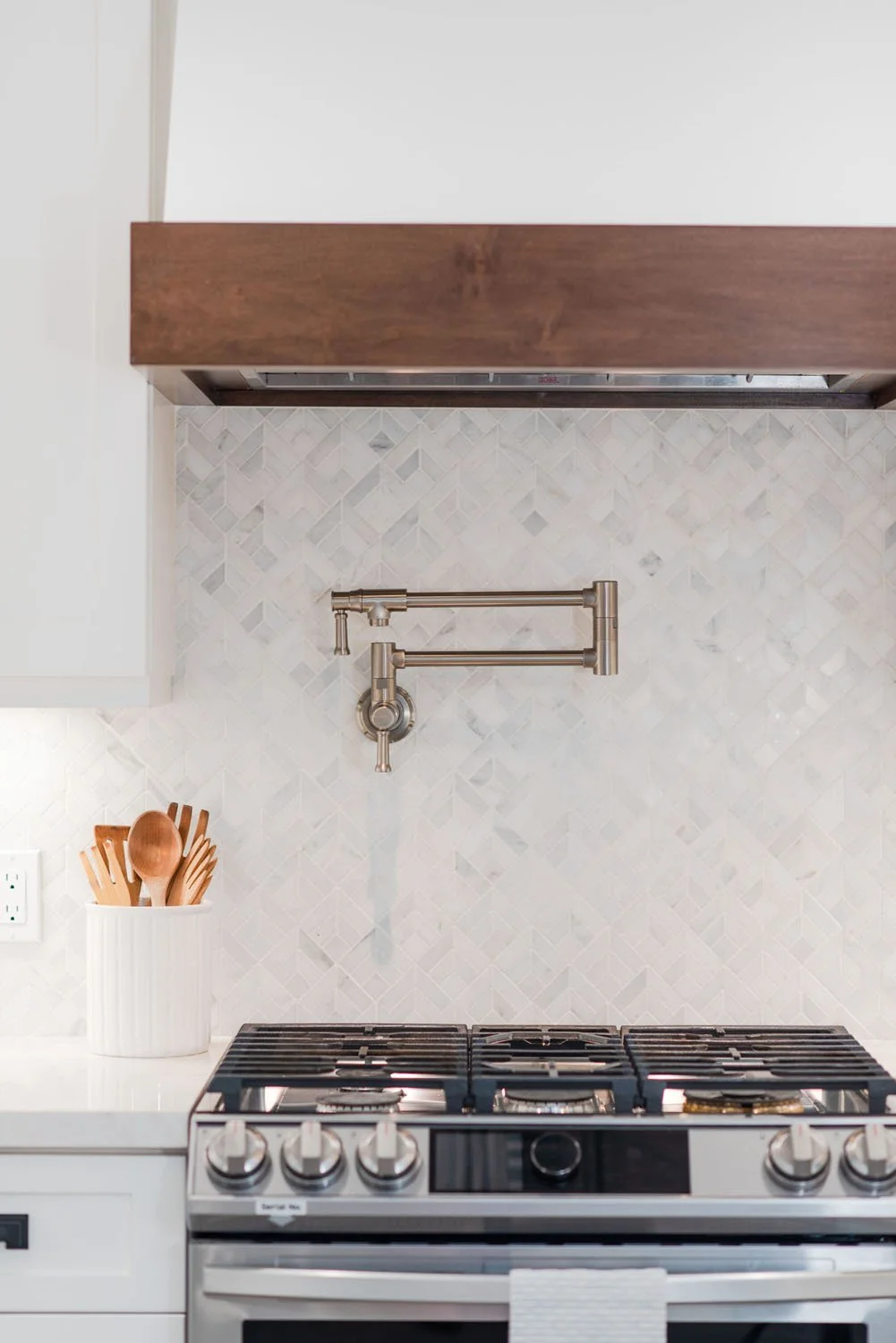 Gas range with walnut hood trim, pot filler and marble herringbone backsplash