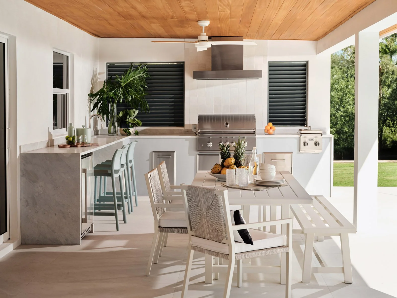 Covered outdoor kitchen with bar stools, dining table and wood ceiling