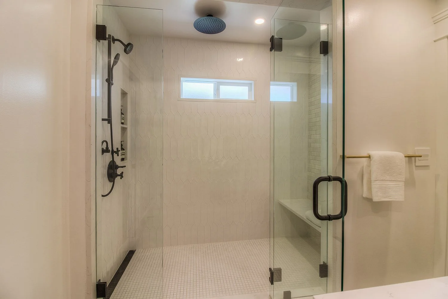 Glass walk-in shower with black fixtures and bench