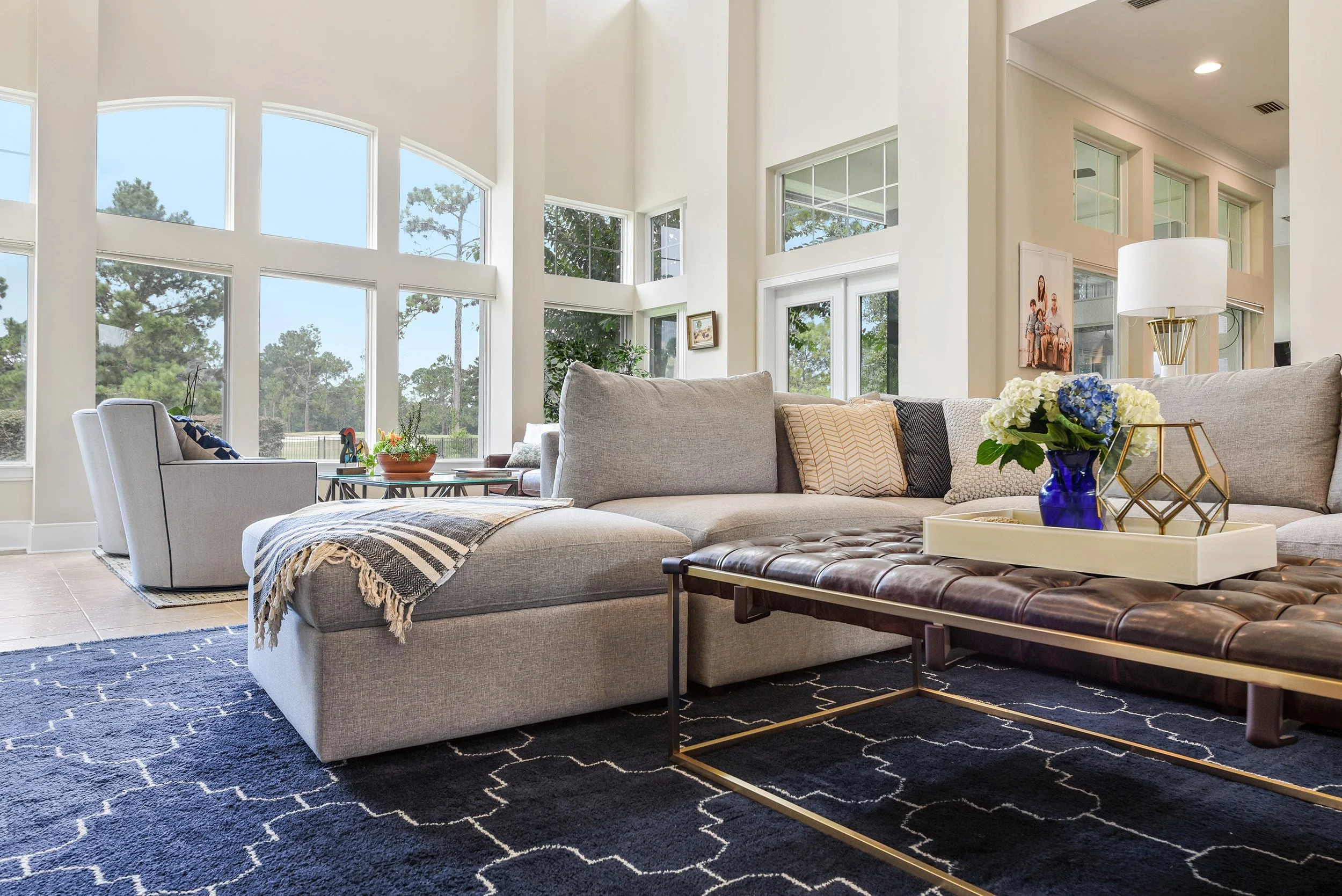 Great room with gray sectional, navy rug and tall windows