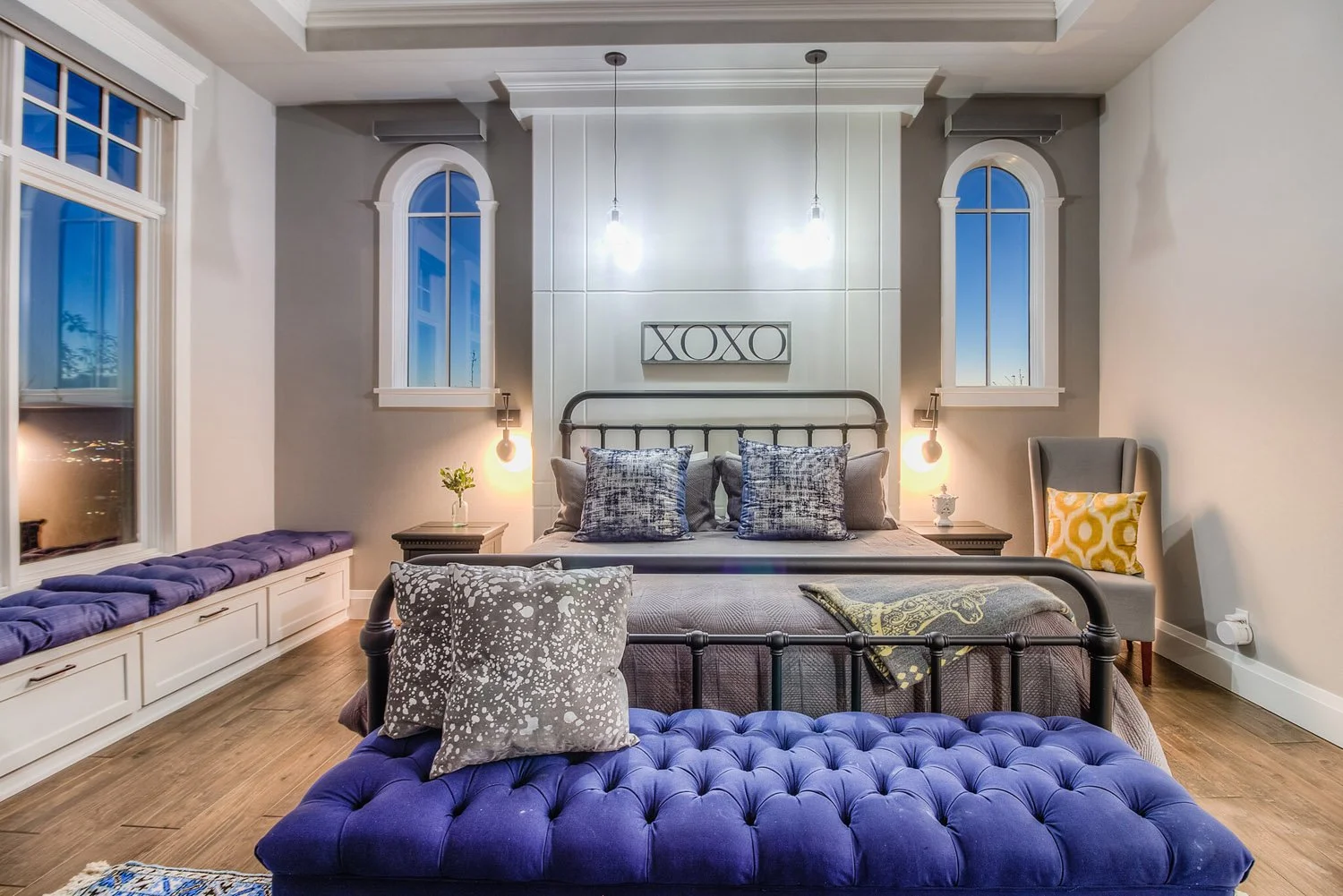 Bedroom with iron bed, navy tufted bench and arched windows