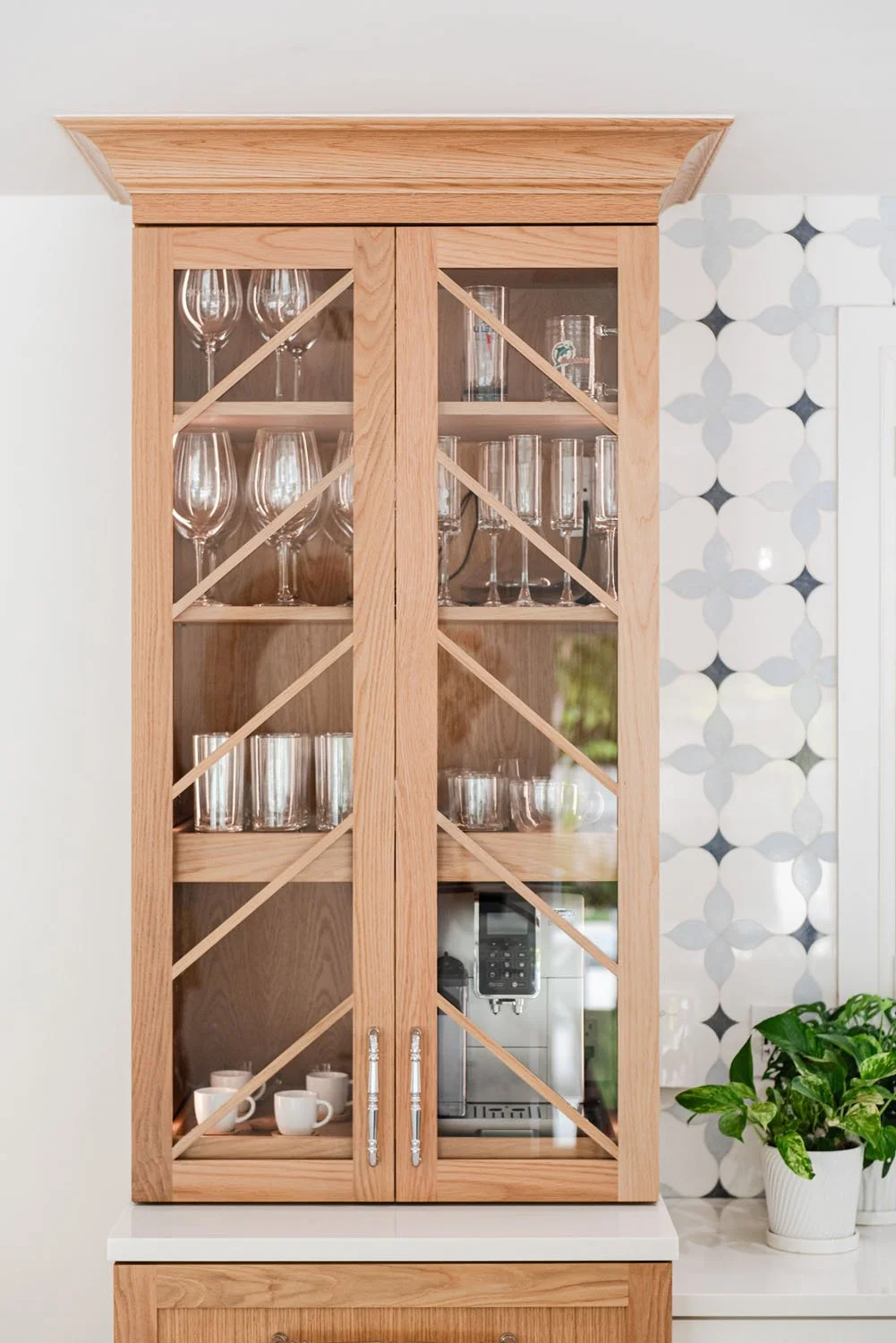 Light wood glass-front hutch with glassware and patterned tile