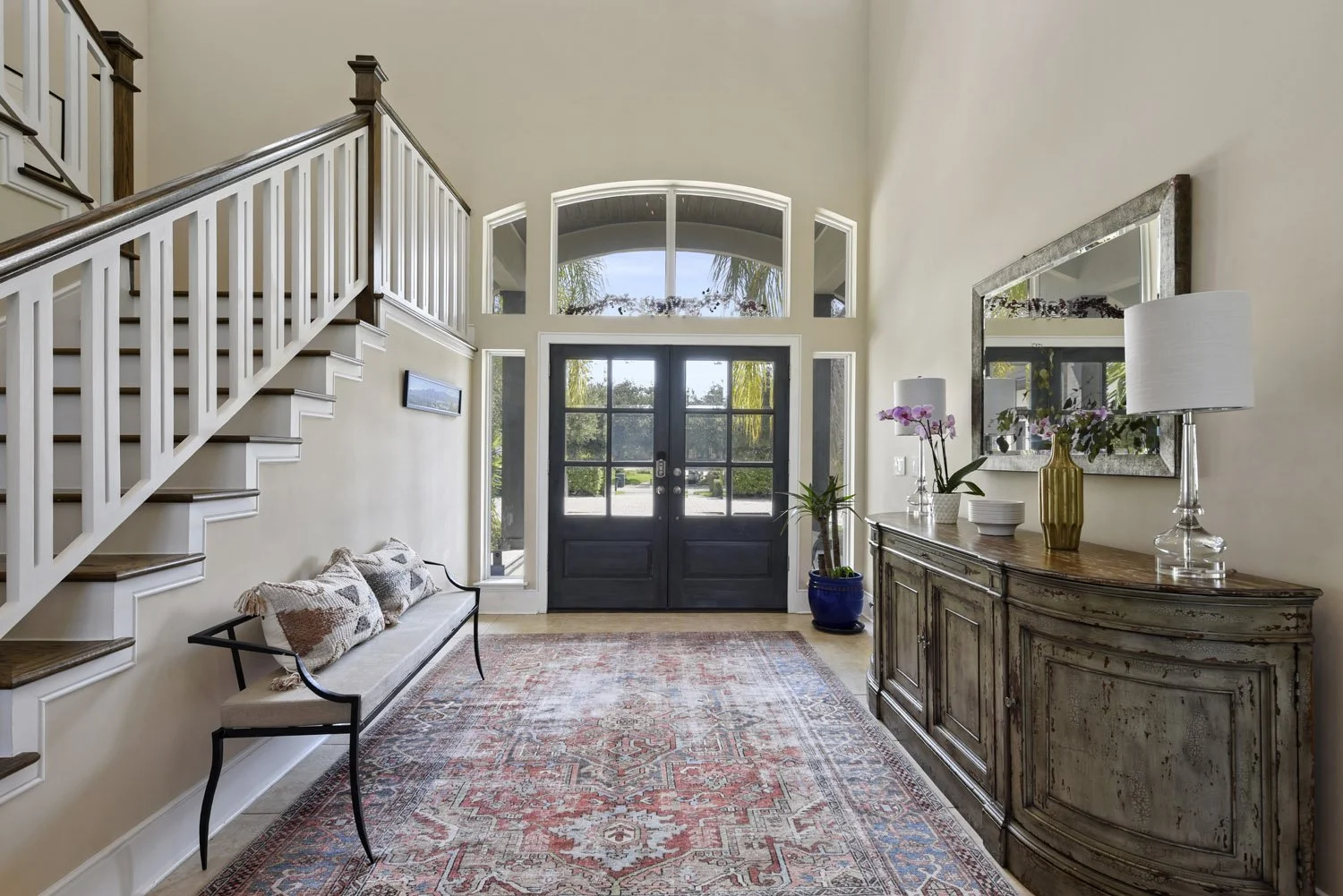 Foyer with white staircase, upholstered bench and red rug