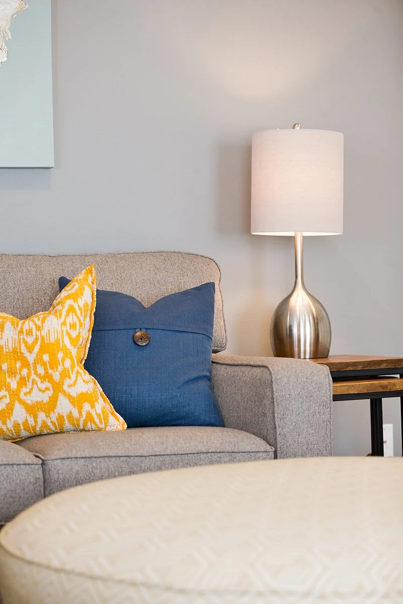Gray sofa with yellow and blue pillows beside a table lamp