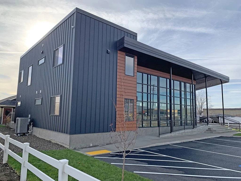 Dark metal-clad building exterior with wood accent and parking lot