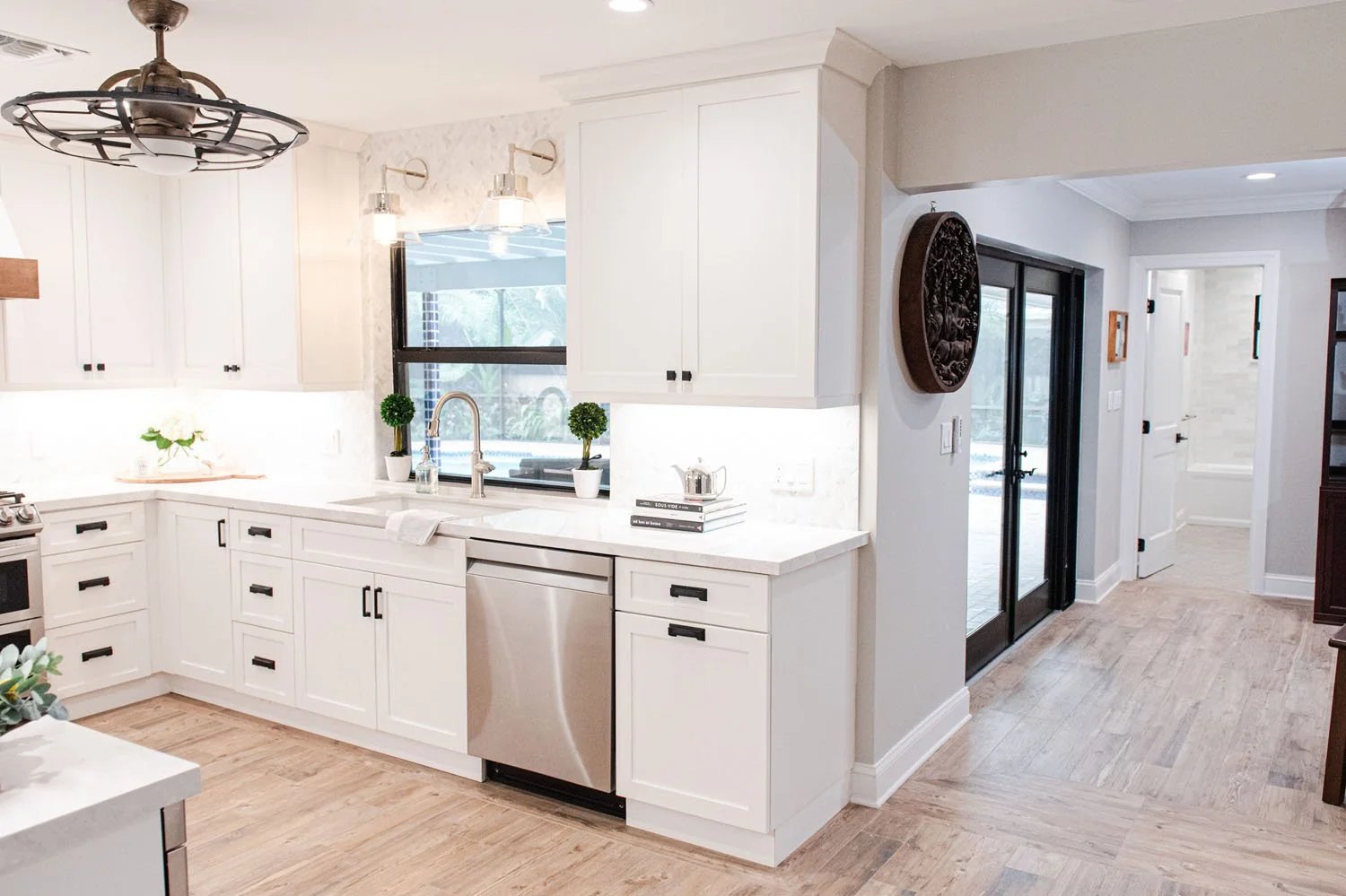 White kitchen opening to living area with ceiling fan