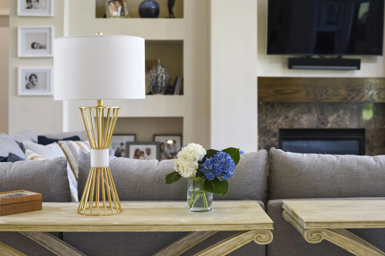 Console table with gold lamps and hydrangeas behind a gray sectional