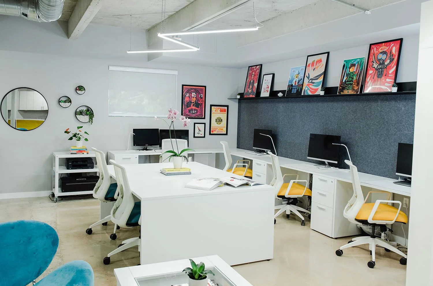 Office with white desks, yellow chairs and framed posters