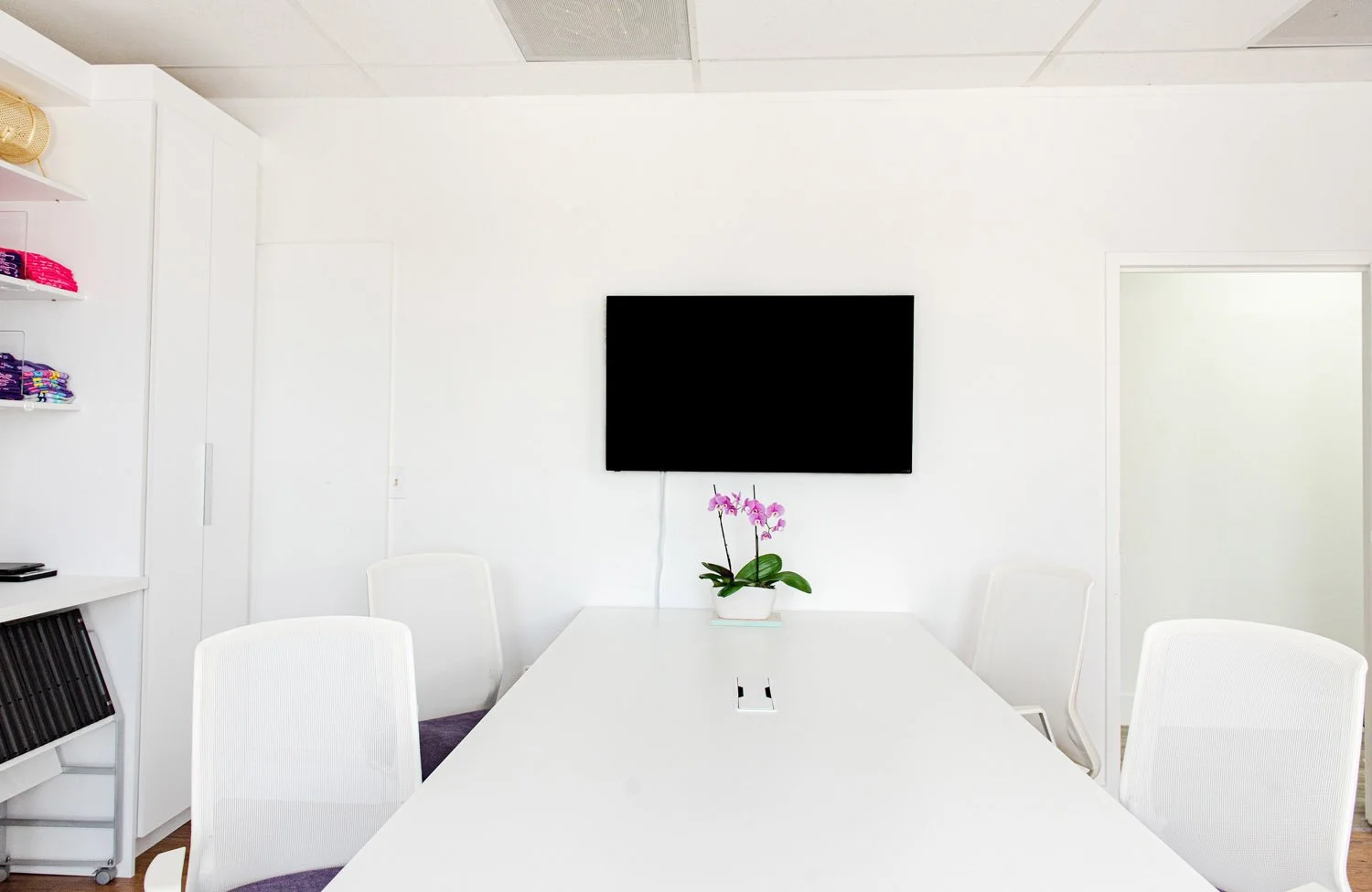 White conference table with chairs facing a wall-mounted TV