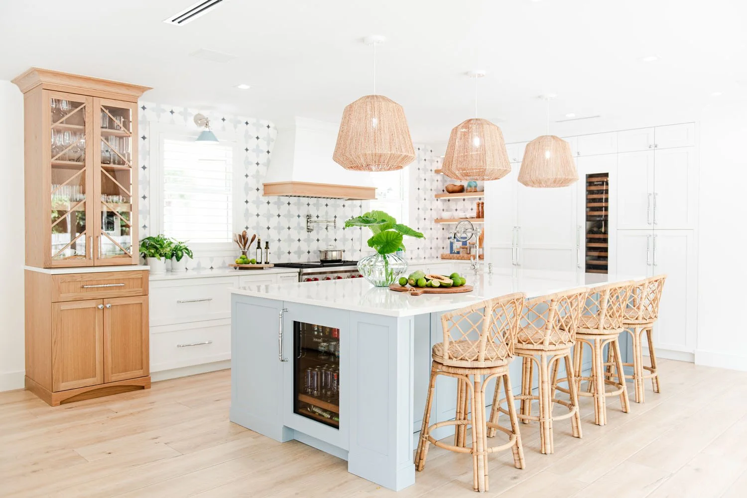 White kitchen with light blue island, rattan pendants and woven counter stools