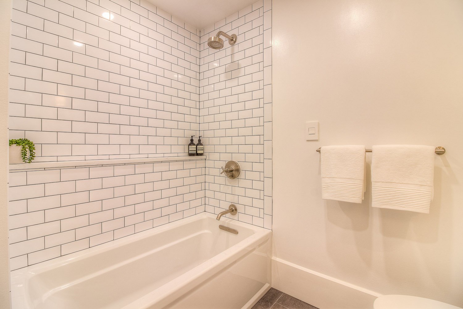 Tub with subway tile and white towels on a hook rail