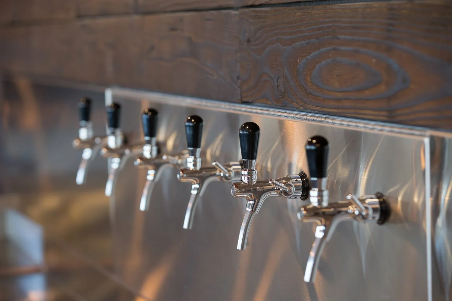 Row of stainless beer taps on a wood-paneled wall