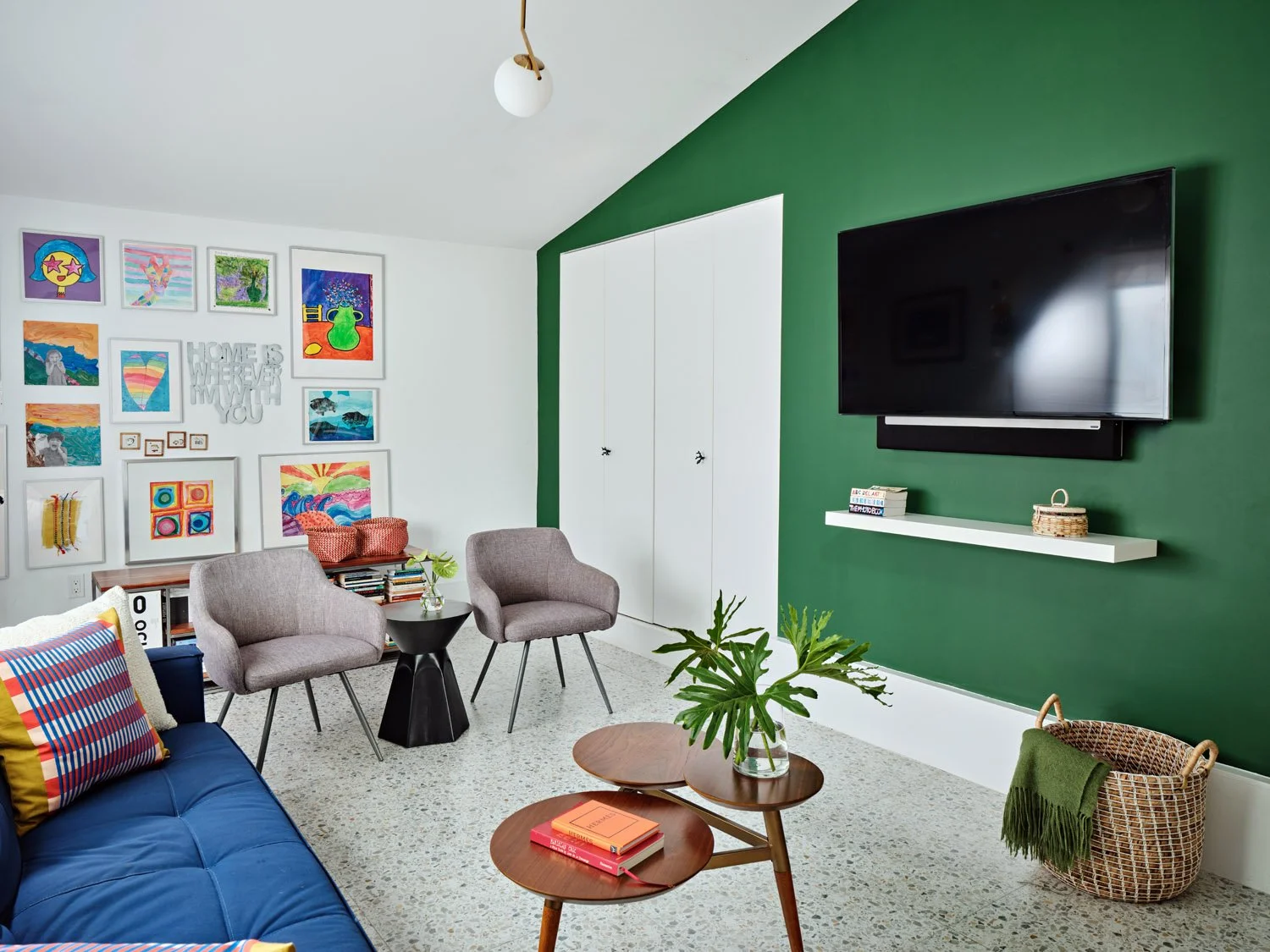 Family room with navy sofa, gray chairs and green accent wall with TV