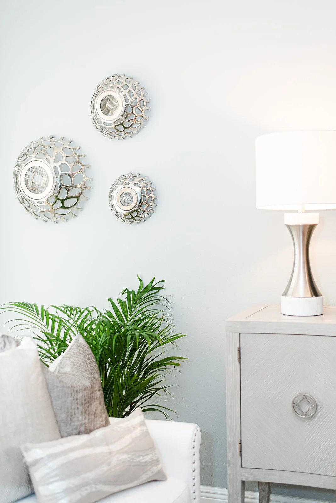 Silver wall medallions above a white chest with potted palm