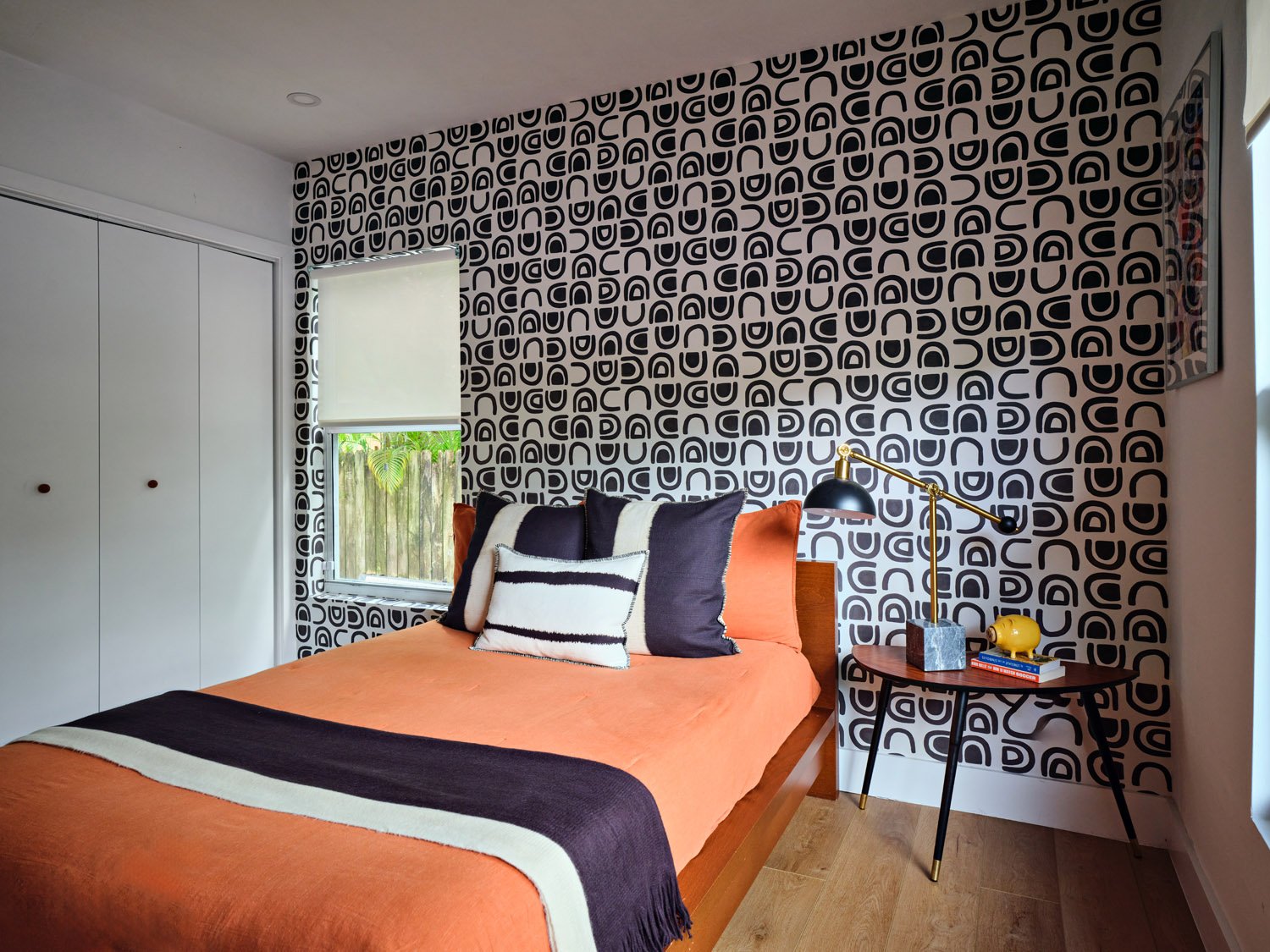 Kids bedroom with patterned wallpaper, orange bedding and side table