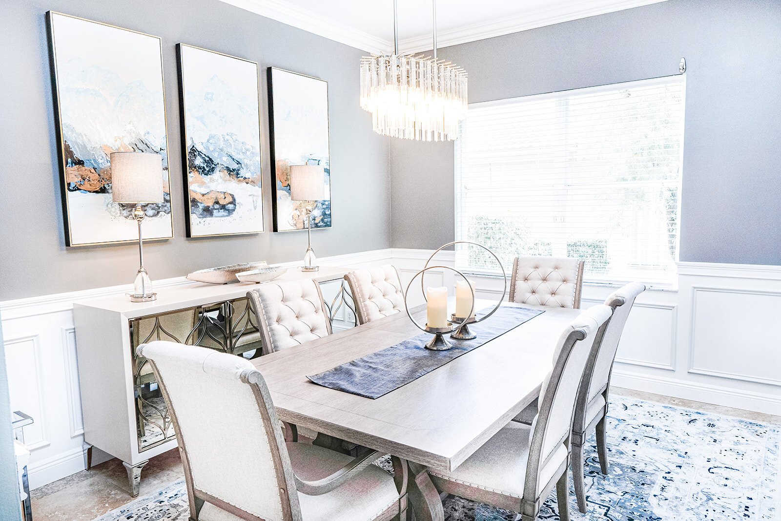 Dining room with crystal chandelier, upholstered chairs and abstract art triptych