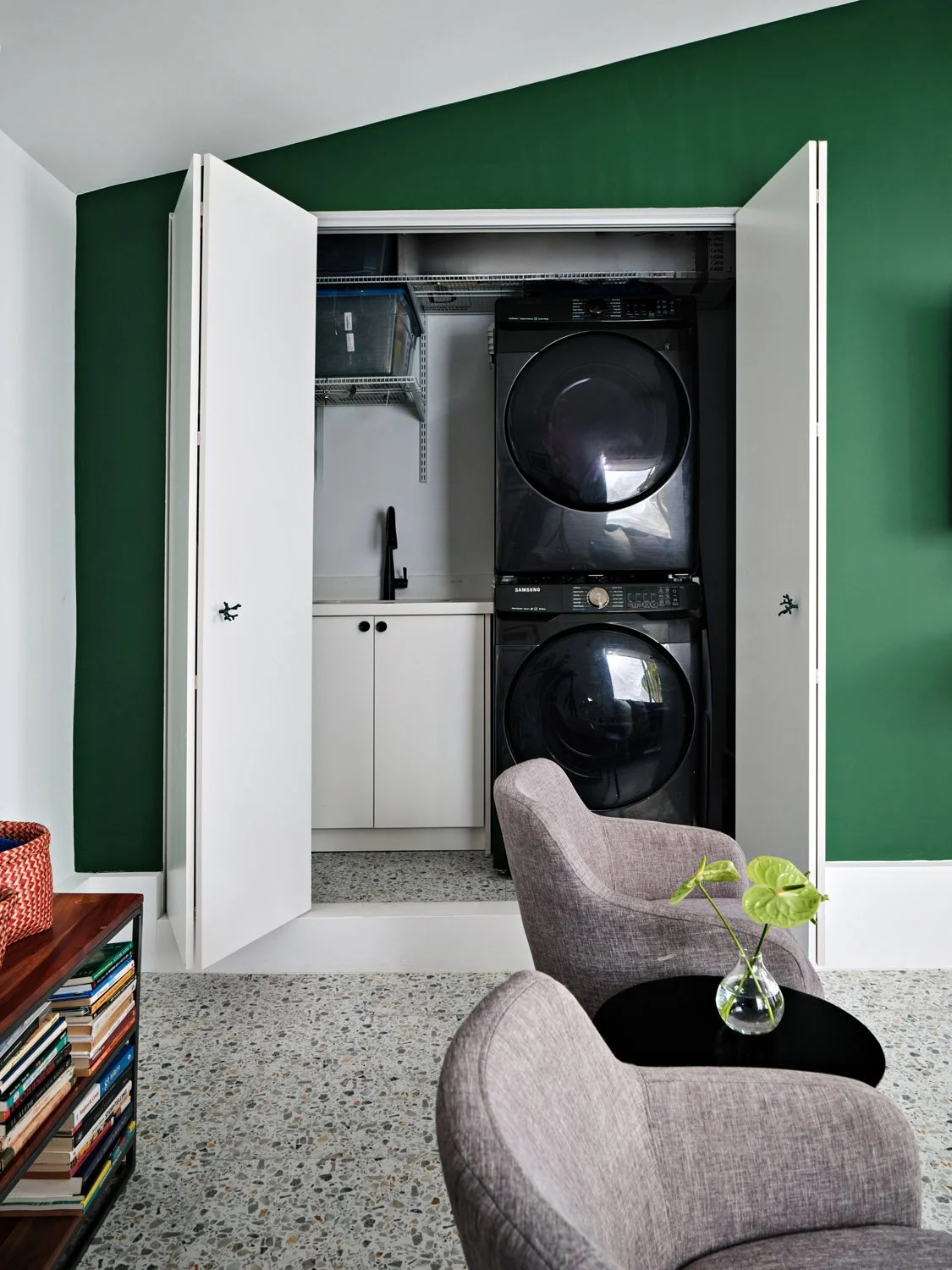Laundry closet with stacked washer and dryer behind green wall