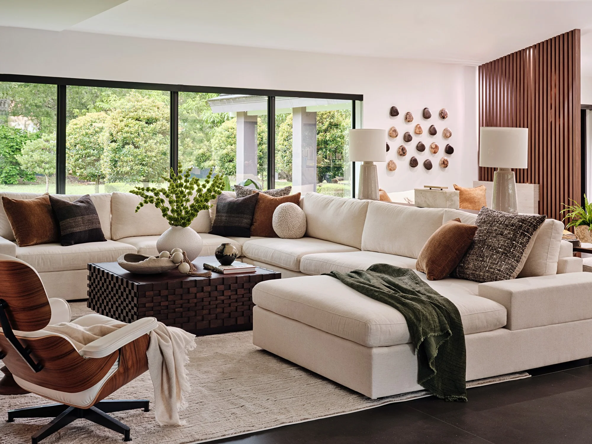 White sectional with green throw, Eames-style lounge chair and walnut wall panel
