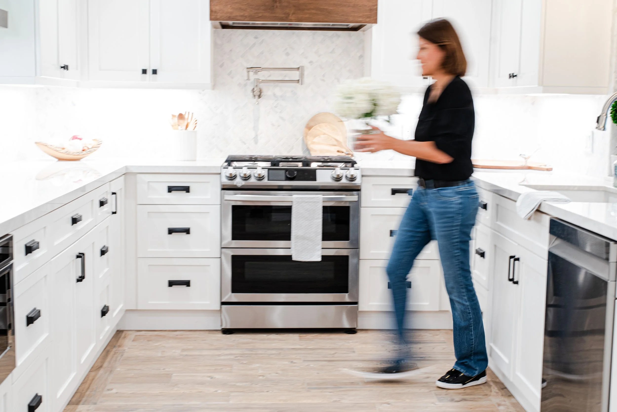 Woman standing at a stainless range in a white kitchen