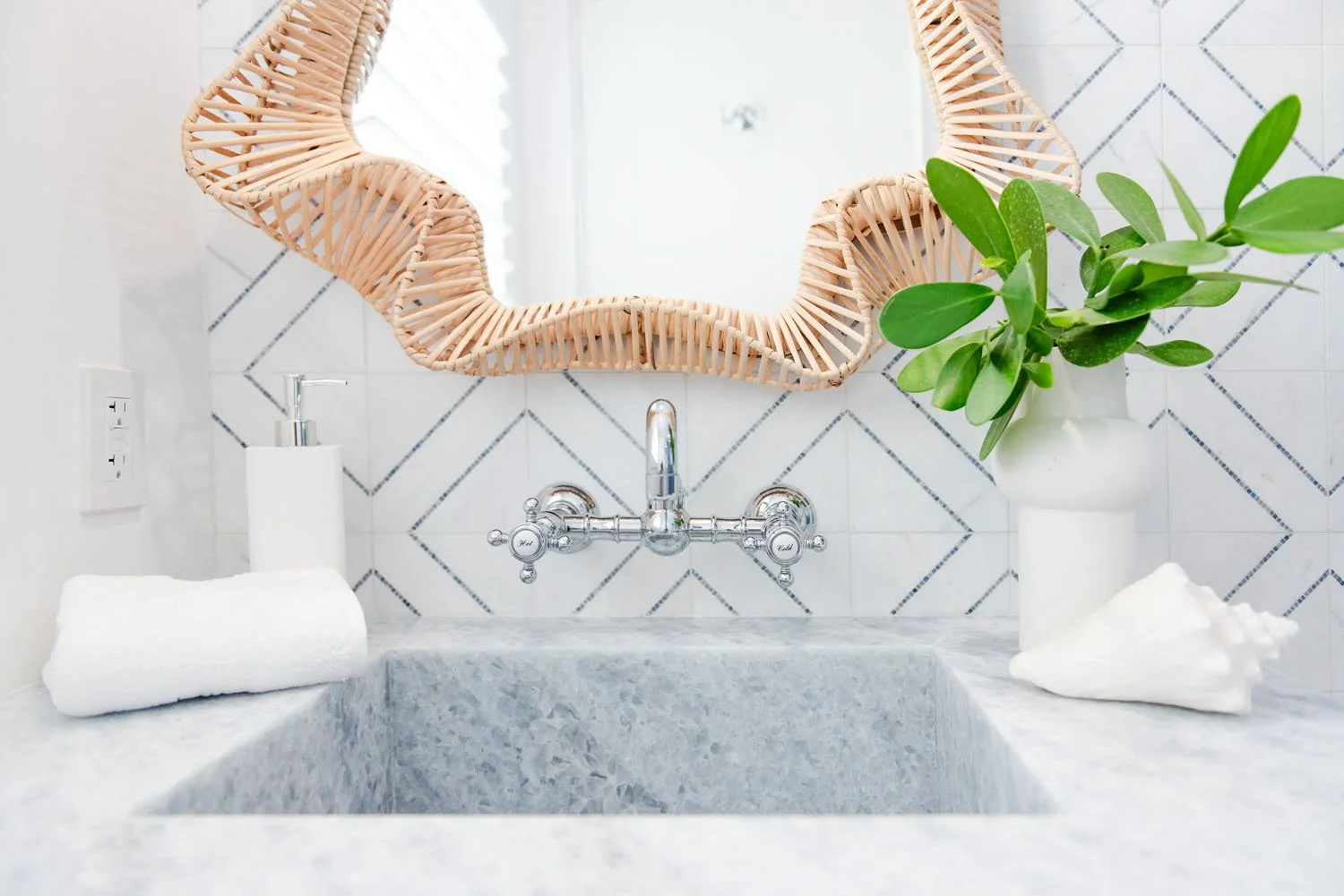 Rattan scalloped mirror above a marble sink with wall-mounted faucet