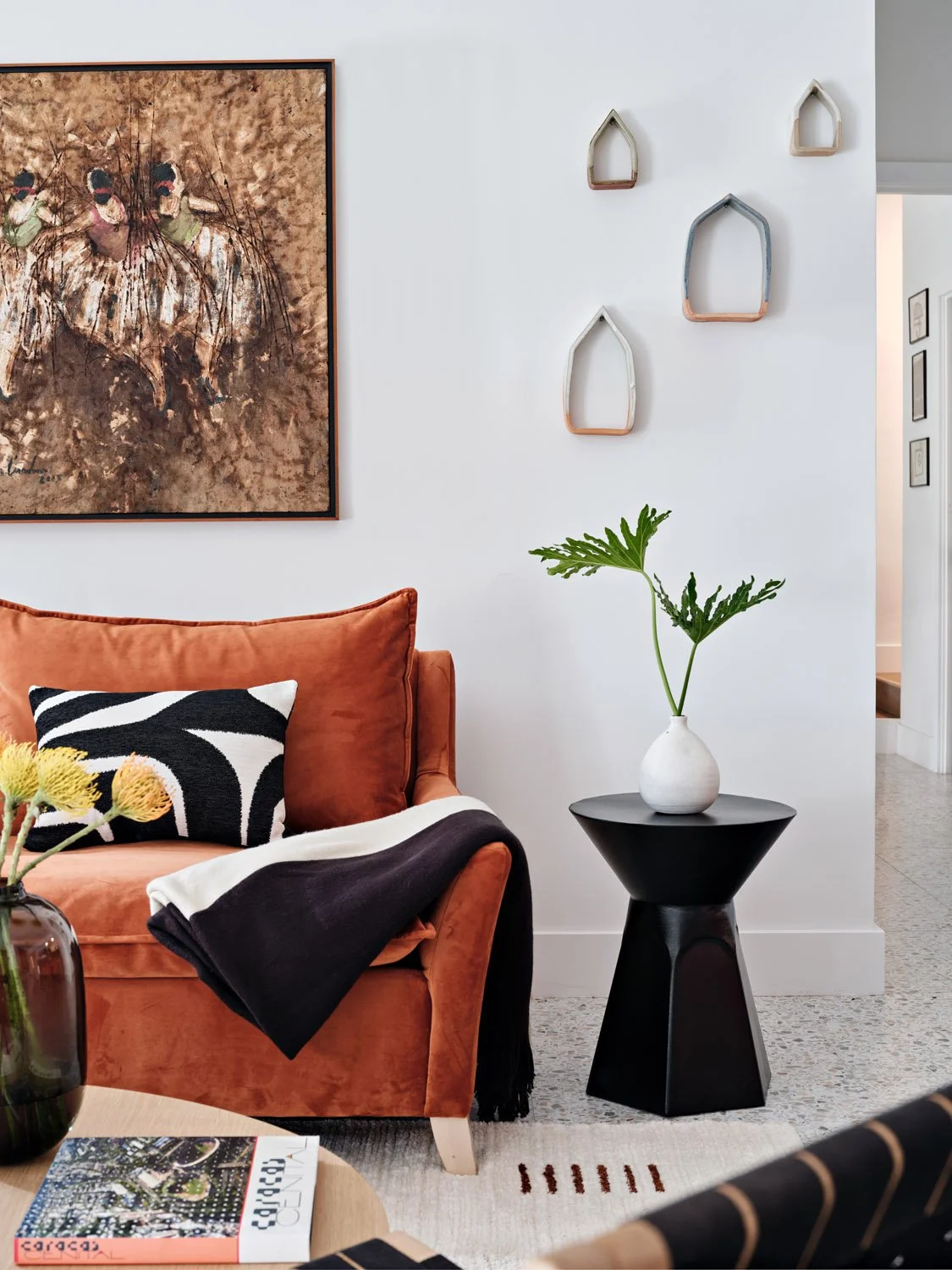 Rust velvet sofa with black side table and abstract wall art