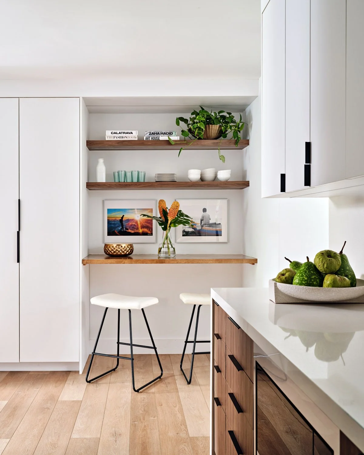Kitchen with floating wood shelves, white stools and walnut cabinetry