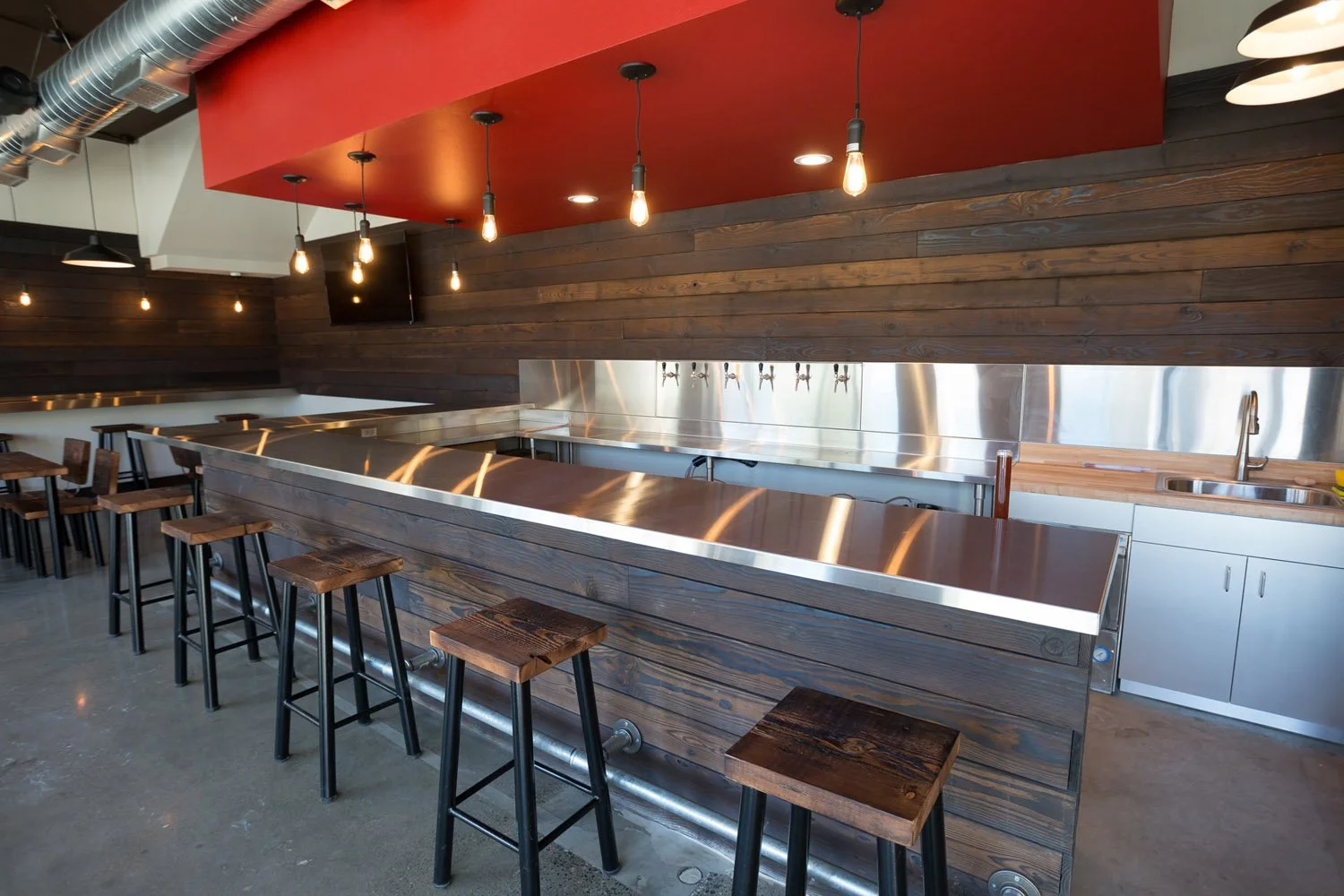 Long stainless bar with wood stools under a red soffit