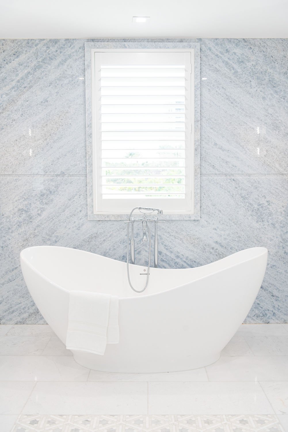 Freestanding white tub against a gray marble wall
